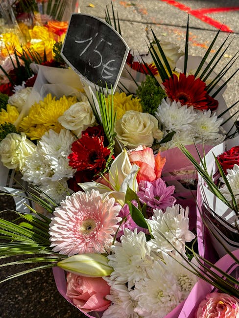 A vibrant floral arrangement consisting of white roses, pink gerbera daisies, deep red gerbera daisies, white lilies, and purple chrysanthemums, all accented with green palm leaves and long, slender l