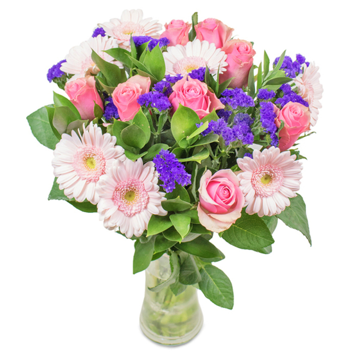 Displayed in a sleek clear glass vase and photographed against a crisp white backdrop, this thoughtfully composed bouquet is a vibrant celebration of pinks and purples. Approximately seven to nine medium and blush pink roses serve as the central focus, each bloom meticulously positioned with some still tightly furled, creating dynamic texture and the classic spiral shape that signals freshness and romance. Nestled amongst these are five to seven pale pink gerbera daisies, easily recognized by their broad, rounded heads and radiant petals that seem to draw in the light-evoking the playful spirit of garden beds around Charlton Lido. Clusters of bold purple statice weave through the bouquet, introducing an eye-catching pop of colour and a papery texture that stands out against the softness of the roses. Deep green foliage frames the arrangement, providing a lush, abundant feel and hinting at verdant walks through Sutcliffe Park. The water-filled vase not only supports but visibly nourishes the stems, emphasizing the bouquet's freshness-perfect for a special birthday, anniversary, or a thoughtful surprise delivered anywhere in Charlton SE7. This arrangement speaks of joy, celebration, and the heartfelt artistry characteristic of the local flower community.